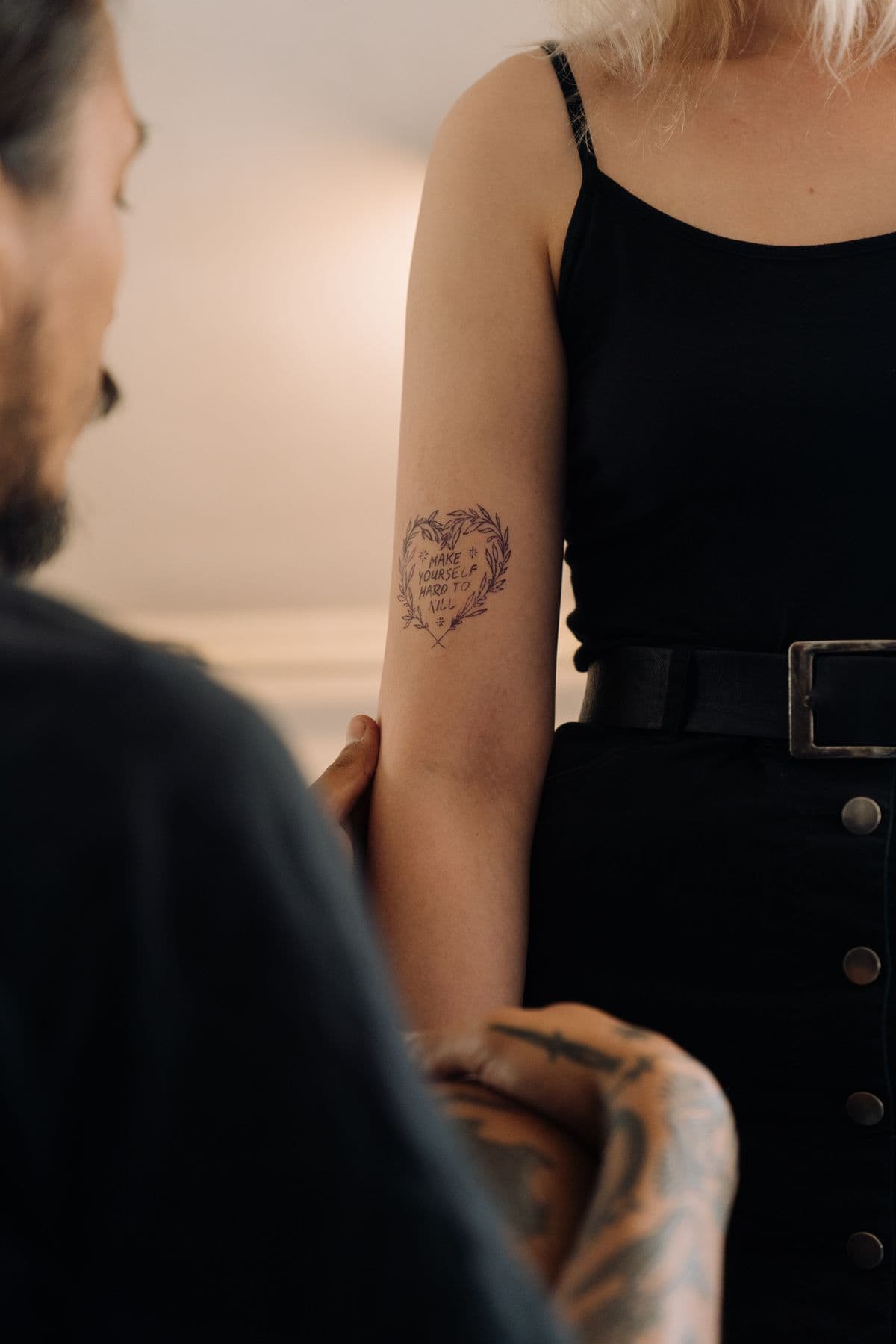 Fine line heart wreath with hand-lettered text on the back of an upper arm